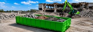 Grüner Abrollcontainer mit sortierten Abbruchabfällen wie Beton, Ziegeln und Metall auf einer Rückbaustelle mit Bagger. @ 